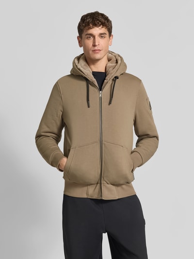 Männermodel trägt Sweatjacke aus Baumwoll-Mix von Moose Knuckles in Beige mit Plüsch-Innenfutter, Reißverschluss und Känguru-Tasche, körpernahe Passform, Nahaufnahme Oberkörper.