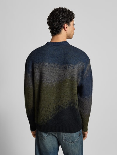 Männermodel trägt Strickpullover mit Rundhalsausschnitt Modell 'TINLEY' von Carhartt Work In Progress, mehrfarbig, grobe Textur, Ganzkörperansicht Rückansicht. Material-Mix mit Alpaka-Anteil, gerader Schnitt, Rückenlänge bei Größe M 72 cm, Ärmellänge 79 cm.