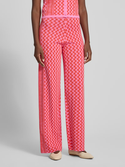Frauenmodel trägt Flared Cut Hose aus Viskose-Mix im Allover-Look Modell 'JONAS' von SUNCOO PARIS, rosa und rot gemustert, elastischer Bund, Ganzkörperansicht von vorne. Damen Hose, Bundweite 35 cm, Innenbeinlänge 28 cm, Größe S.