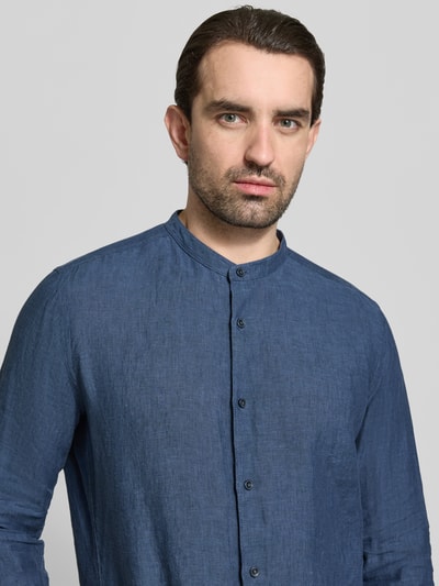 Männermodel trägt Slim Fit Leinenhemd aus reinen Leinen mit Stehkragen von OLYMP, Knopfleiste, Langarm, blaue Textur, Nahaufnahme Oberkörper.