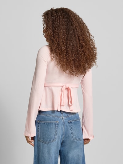 Frauenmodel trägt Regular Fit Langarmshirt in Wickel-Optik Modell 'PELLY' von Only mit Struktur-Muster, Bindeband, Trompetenärmel, Ganzkörperansicht Rückansicht.