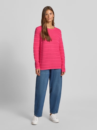Frauenmodel trägt Regular Fit Pullover aus reiner Baumwolle in Strick-Optik von Christian Berg Woman in Pink, semitransparent, Rundhalsausschnitt, kombiniert mit blauer Jeans und weißen Sneakern, Ganzkörperansicht von vorne.
