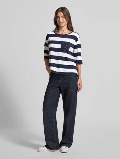 Frauenmodel trägt Relaxed Fit Sweatshirt aus Viskose-Mix mit Brusttasche von monari, marineblau-weiß gestreift, Halbarm, Rundhalsausschnitt, Logo-Stitching, lässige Passform, weiche Textur, kombiniert mit dunkler Jeans, Ganzkörperansicht von vorne.