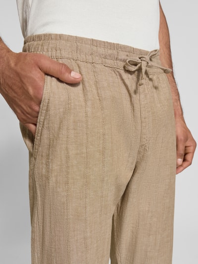 Männermodel trägt Relaxed Fit Hose aus Baumwoll-Leinen-Mix Modell 'KANE' von Jack & Jones in Beige mit elastischem Bund und Tunnelzug, Nahaufnahme Oberkörper; Leinenstruktur und Gesäßtasche, Bundweite 41 cm, Innenbeinlänge 77 cm.