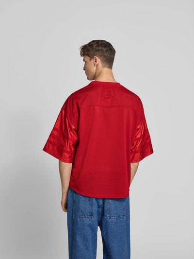Männermodel trägt Relaxed Fit T-Shirt mit 3/4-Ärmel von RHUDE, rotes Mesh und Satin, Rückenlänge 69 cm, Ganzkörperansicht Rückansicht.