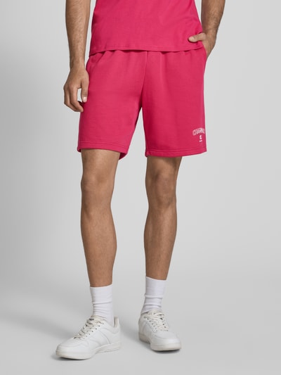 Mannenmodel draagt Sweatshorts mit Logo und elastischem Bund van CHAMPION, regular fit, katoenmix, elastische tailleband, tunnelkoord, felroze kleur, korte broek met logo op de pijp, productkenmerken volgens context, vooraanzicht halflichaam.