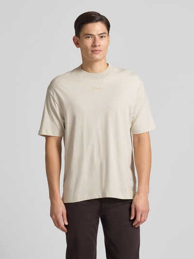 Männermodel trägt T-Shirt mit Label-Detail von Guess in Beige, Reine Baumwolle, Lockerer-Schnitt, Gerippter Rundhalsausschnitt, Ganzkörperansicht von vorne. Rückenlänge bei Größe M: 73 cm.