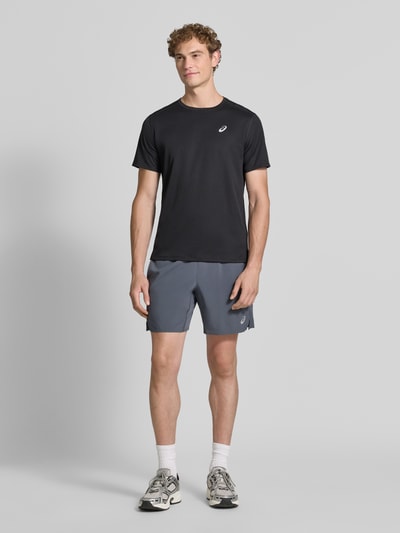 Męski model nosi Regular Fit Shorts mit integriertem Slip Modell 'Core' von ASICS TIGER, szare, nadruk z logo, elastyczny pas, Szerokość w rozmiarze M: 38 cm, Długość wewnętrzna nogawki w rozmiarze M: 17 cm, Ganzkörperansicht von vorne.