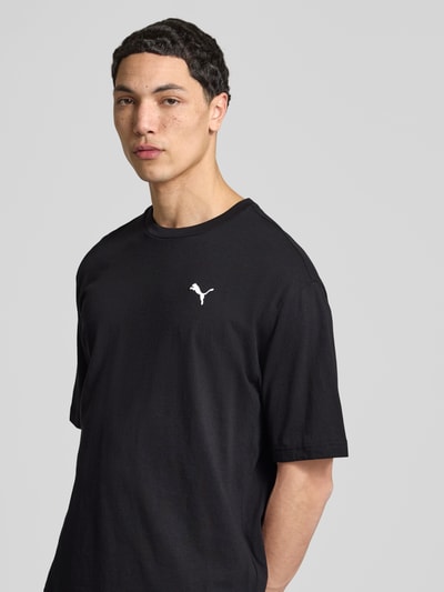 Männermodel trägt T-Shirt mit Rundhalsausschnitt von PUMA PERFORMANCE in Schwarz, Logo auf der Brust, Relaxed Fit, Nahaufnahme Oberkörper.
