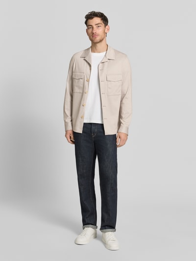 Männermodel trägt Slim Fit Hemdjacke mit Brusttaschen Modell 'Constantin' von CG - Club of Gents in licht beige, katoenmix, reverskraag, voorkant borstzakken, gecombineerd met donkerblauwe jeans en witte sneakers, context heren hemdjacke, viskosemix, ruglengte 72 cm bij maat 50, ganzkörperansicht von vorne.