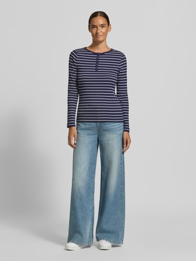 Modelka nosi Slim Fit Langarmshirt aus Baumwoll-Mix mit kurzer Knopfleiste von Christian Berg Woman, krój slim fit, elastyczna bawełniana mieszanka, okrągły dekolt, długie rękawy, długość tyłu w rozmiarze S: 58 cm, granatowe i białe paski; widok całej sylwetki z przodu.