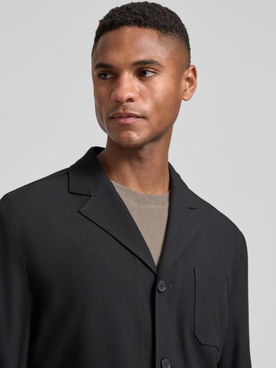 Männermodel trägt Relaxed Fit Hemdjacke mit Viskose-Anteil Modell 'Bill' von DIGEL in Schwarz, strukturierte Oberfläche, Nahaufnahme Oberkörper. Elastischer Material-Mix, Reverskragen, aufgesetzte Tasche, Knopfleiste.