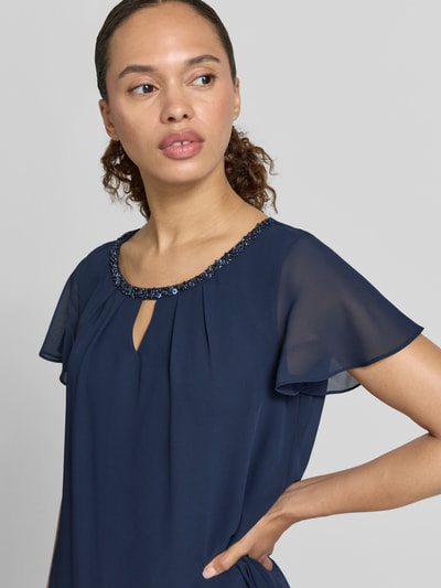 Frauenmodel trägt knielanges Cocktailkleid mit Schlüsselloch-Ausschnitt von Christian Berg Cocktail aus navyfarbenem Chiffon, Stufen-Look, Perlen am Ausschnitt, gerader Schnitt, Nahaufnahme Oberkörper. Rückenlänge bei Größe 36: 93 cm, Brustweite: 47 cm, Ärmellänge: 12 cm.