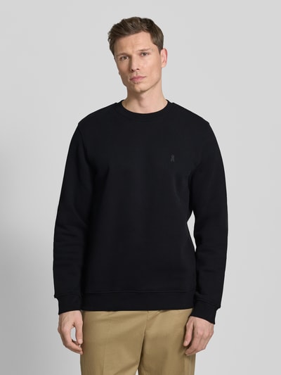 Männermodel trägt Regular Fit Sweatshirt aus reiner Bio Baumwolle Modell 'BAARO FLEECE' von Armedangels, unifarben schwarz, Rundhalsausschnitt, langarm, gerippte Abschlüsse, dezentes Logo-Detail, Sweat-Material, Ganzkörperansicht von vorne.