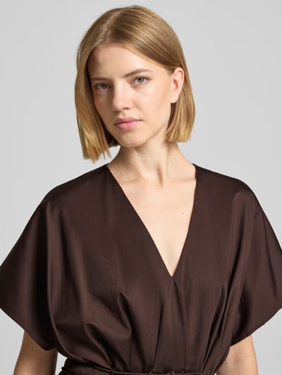 Frauenmodel trägt Cocktailkleid mit V-Ausschnitt und Schnürung von Christian Berg Cocktail in Dunkelbraun, glatte Baumwoll-Elasthan-Textur, Nahaufnahme Oberkörper. Midikleid in A-Linie laut Kontext.