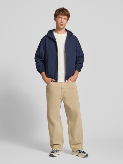 Männermodel trägt Regular Fit Jacke mit Kapuze Modell 'Charge' von JACK & JONES in Dunkelblau, Reißverschluss, beige Hose, Ganzkörperansicht von vorne. Rückenlänge 68 cm, Schulterbreite 50 cm, Brustweite 60 cm, Ärmellänge 66 cm.
