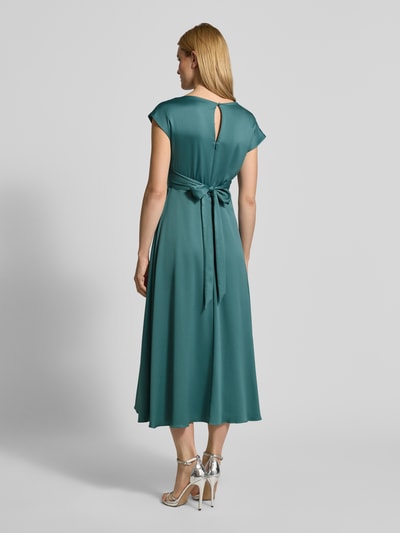 Frauenmodel trägt Relaxed Fit Midikleid mit Stoffband von Christian Berg Cocktail in Satin, grün, gerader Ausschnitt, Ganzkörperansicht Rückansicht.