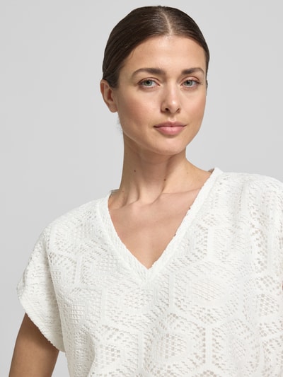 Kobiece model prezentuje Boxy Fit T-Shirt mit semitransparentem Besatz Modell 'IRIS' od Vero Moda, efekt: jednolity kolor, abstrakcyjny wzór, dekolt w serek, bez rękawów, wykończenie materiału: ażur, stretch, półprzezroczyste obszycie, zbliżenie na górną część ciała.