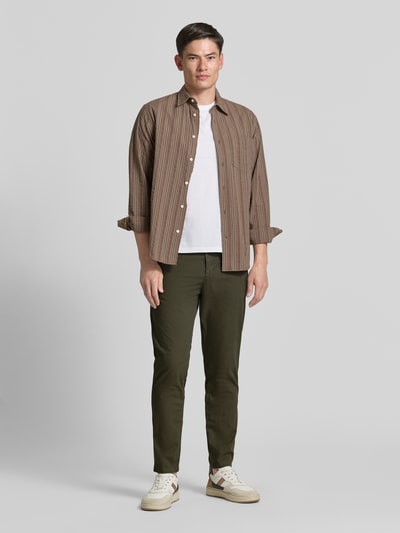 Męski model nosi Tapered Chino aus Baumwoll-Mix Modell 'CHINO-TAPERED-DS-10' od BOSS Orange, kolor jednolity, krój tapered, bawełniany materiał, przód z guzikami i paskiem, kieszenie boczne i tylne, widok całej sylwetki z przodu.