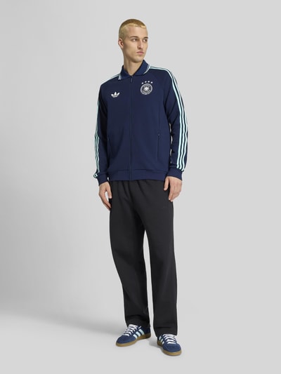 Männermodel trägt Regular Fit Trainingsjacke mit Deutschland Logo von adidas Sportswear, Optik: Unifarben, Ganzkörperansicht von vorne.