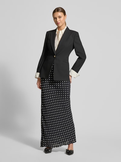 Frauenmodel trägt Maxirock mit blickdichtem Unterrock Modell 'Viso' von Neo Noir, schwarze Grundfarbe mit weißen Punkten, strukturierte Stoffoptik, kombiniert mit Blazer und Bluse, Ganzkörperansicht von vorne. Bundweite 39 cm, Gesamtlänge 111 cm bei Größe 36.