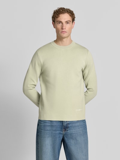 Męski model nosi sweter z mieszanki wiskozy z dodatkiem streczu Samsøe Samsøe Pullover aus Viskose-Mix mit Label-Stitching Modell 'MATT', krój slim fit, okrągły dekolt, wyhaftowane logo, jasny kolor, gładka struktura, długość tyłu w rozmiarze M: 67 cm, długość rękawów w rozmiarze M: 68 cm. Ganzkörperansicht von vorne.
