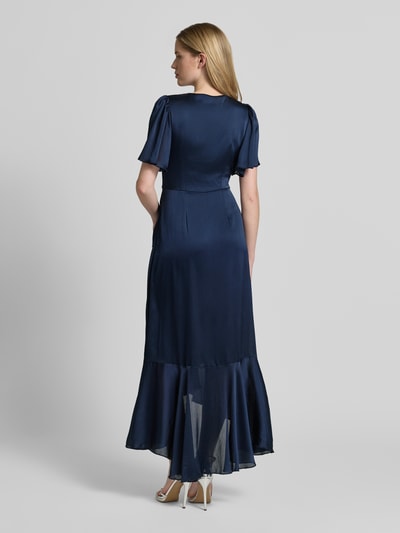 Frauenmodel trägt Cocktailkleid in Wickel-Optik mit V-Ausschnitt von Lipsy, dunkelblauer Satin, Volantsaum, taillierter Schnitt, Maxikleid, blickdichtes Unterkleid, Ganzkörperansicht Rückansicht.