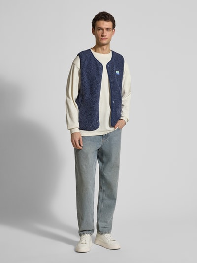 Männermodel trägt Straight Fit Weste mit Logo-Patch Modell 'Hoktown' von American Vintage in Dunkelblau aus Kunstfell, Ganzkörperansicht von vorne.