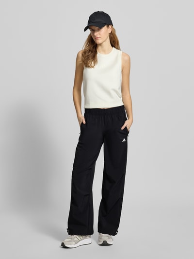 Frauenmodel trägt Wide Fit Stoffhose mit Logo-Print von adidas Sportswear in Schwarz, elastischer Bund, lockerer Schnitt, Ganzkörperansicht von vorne.