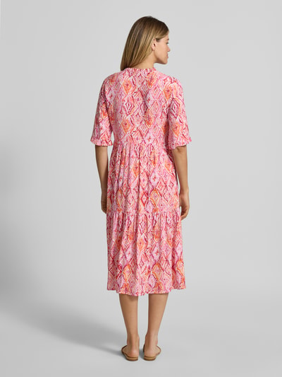 Frauenmodel trägt Ausgestelltes Maxikleid aus reiner Viskose Modell 'EASY JOY' von Vero Moda, Optik:Allover-Muster, Maxi-Länge, Henley-Ausschnitt, Raffung, Verschluss:Knopfleiste, Ärmelform:1/2-Arm, Saum:Gerade, Material:Reine Viskose; Muster aus Rosa, Pink und Orange, fließende Textur, Ganzkörperansicht Rückansicht.