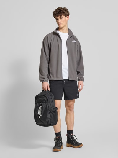 Männermodel trägt Fleecejacke mit Label-Stitching von The North Face in Grau, kombiniert mit Shorts, Reißverschluss, Ganzkörperansicht von vorne.