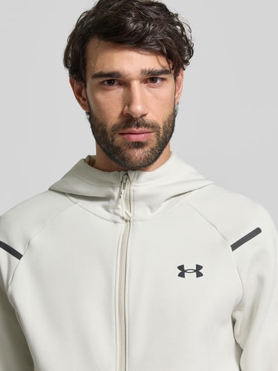 Männermodel trägt Regular Fit Jacke mit Kapuze Modell 'Unstoppable' von Under Armour, Logo-Print, Zweiwege-Reißverschluss, Nahaufnahme Oberkörper. Elastischer Material-Mix mit Baumwoll-Anteil im Regular Fit, geteilte Känguru-Tasche, elastische Abschlüsse, Rückenlänge 75 cm, Ärmellänge 57 cm.