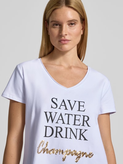 Frauenmodel trägt T-Shirt mit Statement-Print von miss goodlife, weißer Baumwoll-Elasthan-Mix, lockerer Schnitt, V-Ausschnitt, Nahaufnahme Oberkörper.