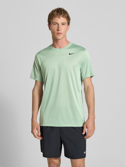 Męski model nosi T-Shirt mit Logo-Print und Rundhalsausschnitt od NIKE TRAINING, krój regular fit, jasna zieleń, prosty fason, całkowita długość 66 cm w rozmiarze M, widok całej sylwetki z przodu.
