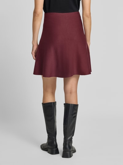Vrouwenmodel draagt Ausgestellter Mini-Rock uit viscosemix van Jake*s Collection in bordeauxrood, gladde textuur, volledige lichaamsopname achteraan.
