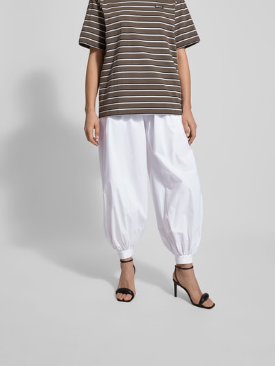 Frauenmodel trägt Stoffhose mit elastischem Bund von ROTATE, reine Baumwolle, lockerer Schnitt, Weiß, Nahtreißverschluss, Nahaufnahme Unterkörper.