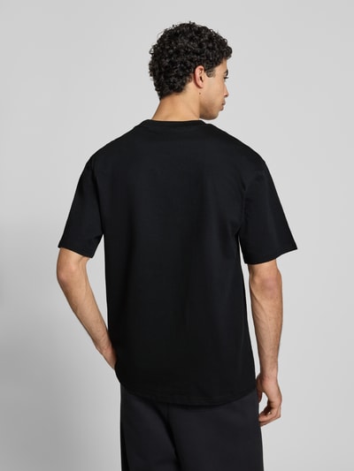 Männermodel trägt Oversized Fit T-Shirt mit Logo-Print Modell 'Heritage' von KARL KANI aus reiner Baumwolle, Rückenlänge 71 cm, Ganzkörperansicht Rückansicht.