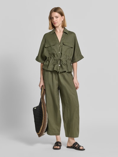 Modelka nosi Leinenhose in verkürzter Passform mit elastischem Bund von Christian Berg Woman, materiał lniany, szerokie nogawki, kolor oliwkowy, szerokość w rozmiarze 36: 38 cm, długość nogawki: 64 cm, widok całej sylwetki z przodu.