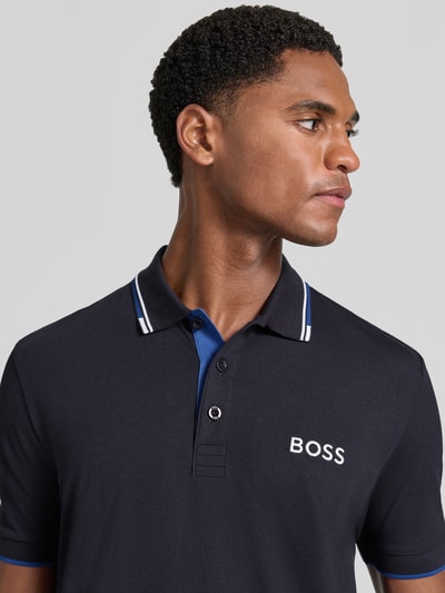 Männermodel trägt Regular Fit Poloshirt aus Baumwoll-Mix Modell ''Paddy Pro'' von BOSS Green in Dunkelblau mit weißem Logo, Nahaufnahme Oberkörper.
