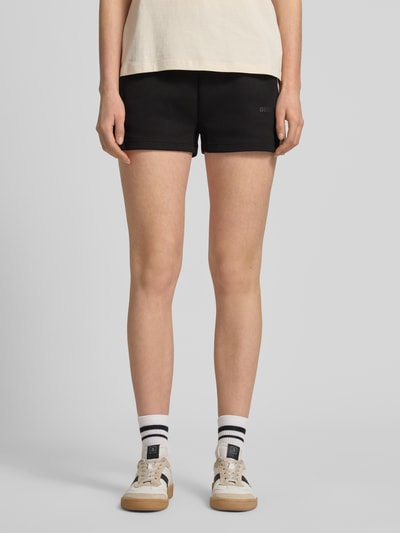Vrouwenmodel draagt Shorts met Kordelzug en Logo-Print Modell 'BRITNEY' van Guess Activewear, katoenmix, loose fit, elastische tailleband met trekkoord, zijzakken, korte zwarte shorts, voorkant volledig in beeld, close-up onderlichaam