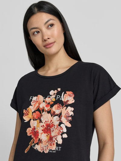 Frauenmodel trägt Damen T-Shirt mit Motiv-Print Modell 'RINA' von Soyaconcept aus Baumwoll-Elasthan-Mix, Regular-Fit, Rundhalsausschnitt, kurzen Ärmeln mit Aufschlag, schwarze Grundfarbe mit buntem Print, Rückenlänge bei Größe S 61 cm, Nahaufnahme Oberkörper.