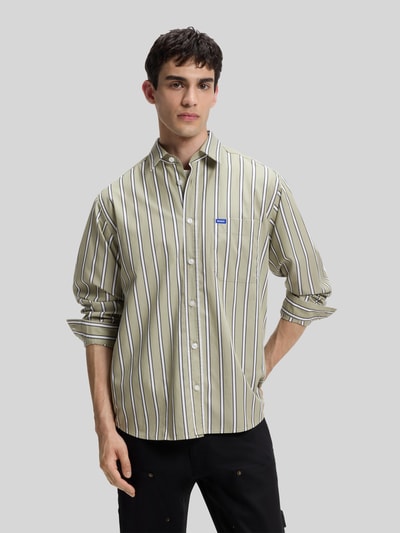 Männermodel trägt Regular Fit Freizeithemd aus reiner Baumwolle Modell 'Ebalto_1' von HUGO Blue mit beigefarbenen und schwarzen Streifen, Ganzkörperansicht von vorne.