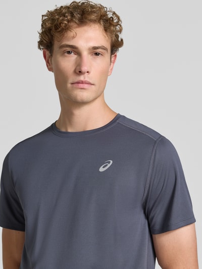 Męski model nosi T-Shirt mit Logo-Print Model 'CORE' von ASICS TIGER w kolorze grafitowym, okrągły dekolt, prosty krój, nadruk z logo, długość tyłu w rozmiarze M: 72 cm, zbliżenie na górną część ciała