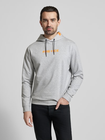 Męski model nosi szarą bluzę z kapturem z logo FIRE + ICE, model 'CADELL', krój regular fit, detal z logo, widok na cały przód.