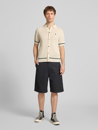 Männermodel trägt Slim Fit Strick-Poloshirt mit Label-Stitching von REVIEW aus Viskose-Mix, Kontraststreifen, Knopfleiste, Ganzkörperansicht von vorne.
