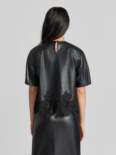 Frauenmodel trägt Blusenshirt in Leder-Optik mit Spitzenbesatz Modell 'LONDON' von SUNCOO PARIS in Schwarz, Ganzkörperansicht Rückansicht. Damen Blusenshirt, Regular Fit, Rundhalsausschnitt, Rückenlänge 55 cm, Ärmellänge 39 cm.