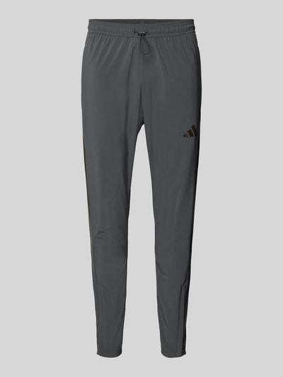 Produktfoto, Regular Fit Jogpants mit elastischem Bund Modell 'TIRO' von adidas Sportswear in Dunkelgrau, schmal zulaufendes Bein, glatte Textur, elastischer Bund mit Kordelzug, Beinabschluss mit Reißverschluss, Seitentaschen, sportlicher Look, für Herren.