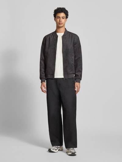 Męski model nosi Regular Fit Blouson in Lederoptik Modell 'LUCAS' von Only & Sons, imitacja skóry, jednolity kolor, długi rękaw, krój regular fit, kołnierz college, zamek błyskawiczny, pas na plecach, wpuszczane kieszenie boczne, kieszeń wewnętrzna, wykończenie materiału: sztuczna skóra, całość w czerni, gładka tekstura, widok całej sylwetki z przodu.