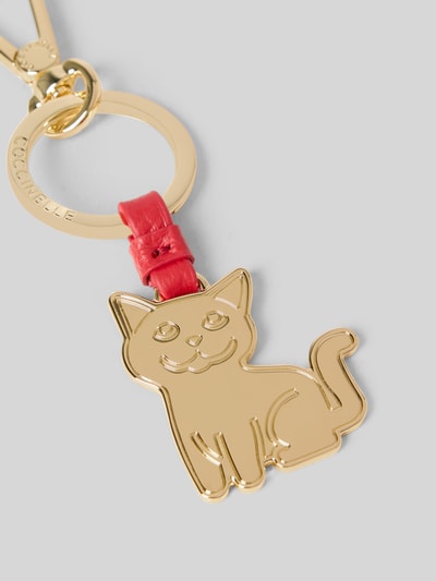 Produktfoto, goldfarbener Katzen-Anhänger mit Logo-Prägung von Coccinelle, Schlüsselring und Verschluss mit Schnapphaken, rote Leder-Details.