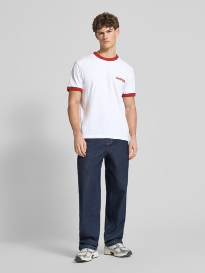 Männermodel trägt T-Shirt im Retro-Look mit Label-Print von Carhartt Work In Progress, weiß mit roten Akzenten, Ganzkörperansicht von vorne